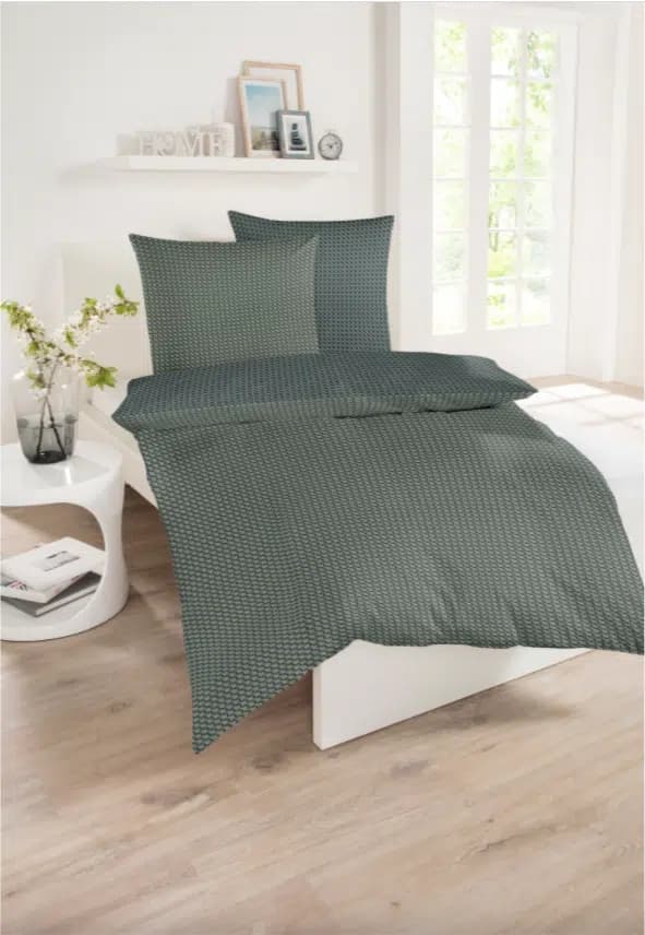 Renforcé-Bettwäsche in Dunkelgrün mit feinem geometrischem Muster auf einem weißen Bett in einem modern eingerichteten, hellen Schlafzimmer.