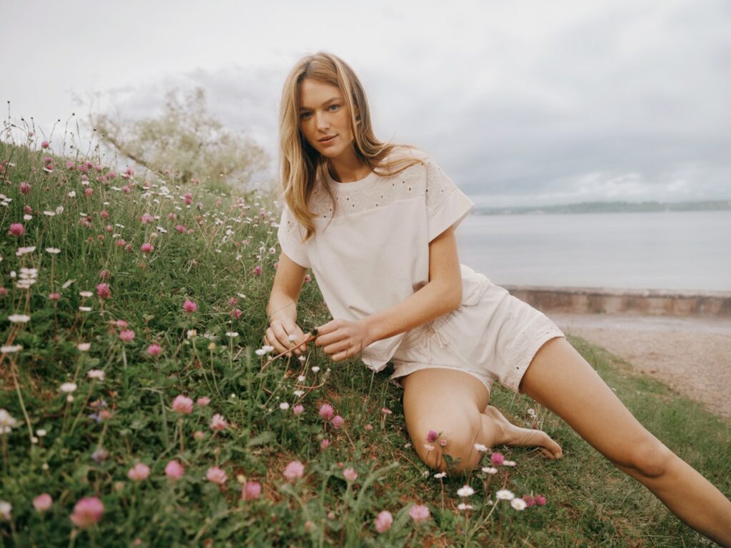 Model in strahlend weißer Wäsche sitzt auf einer blühenden Wiese