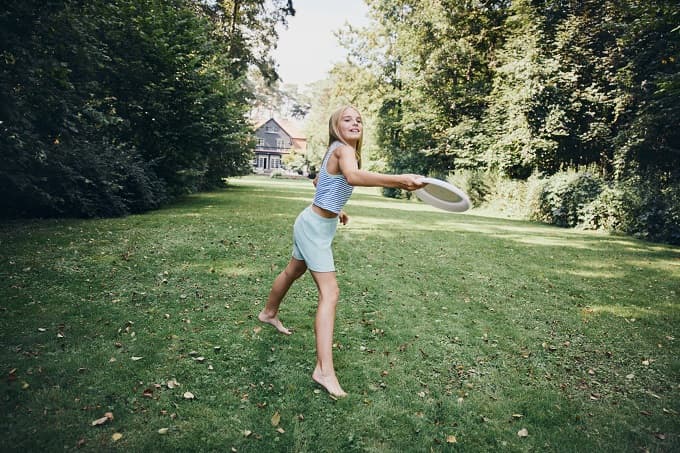 Junges Mädchen spielt Frisbee auf dem Rasen - als Symbol für den ersten BH bei heranwachsenden Mädchen