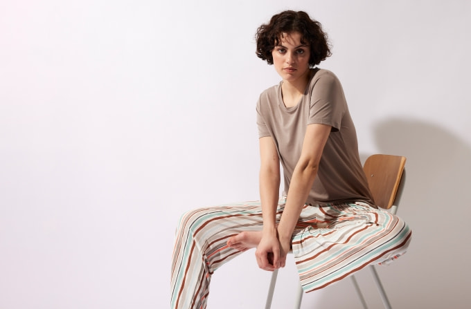 Model in Pyjama - bestehend aus einem T-Shirt und einer langen Hose - sitzt auf einem Stuhl