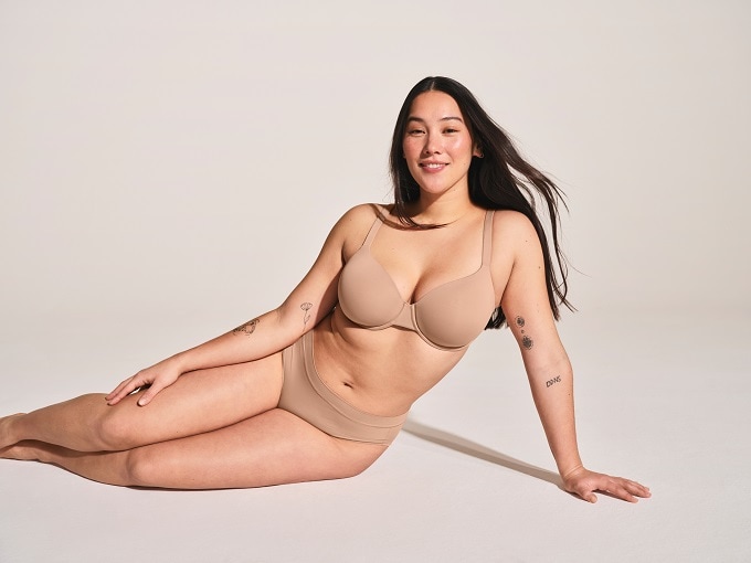 Bustier Microfaser herausnehmbare Pads sand - Invisible Soft Frau in hautfarbener Seamless-Unterwäsche sitzt auf dem Boden – nahtloser BH und Slip für perfekten Sitz ohne Abdrücke, ideal unter enger Kleidung.