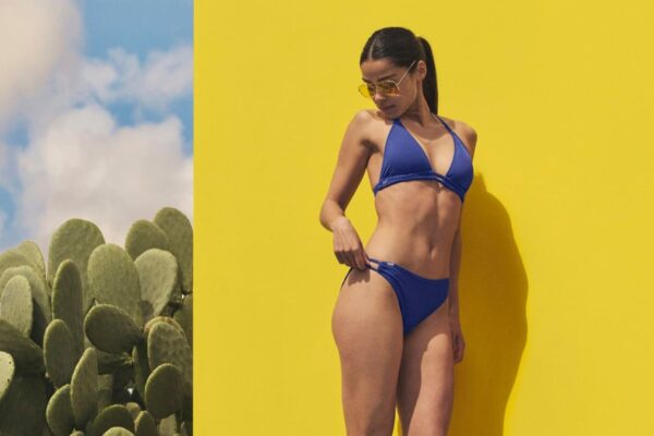 Frau trägt einen blauen Bikini am Pool vor einer gelben Wand.