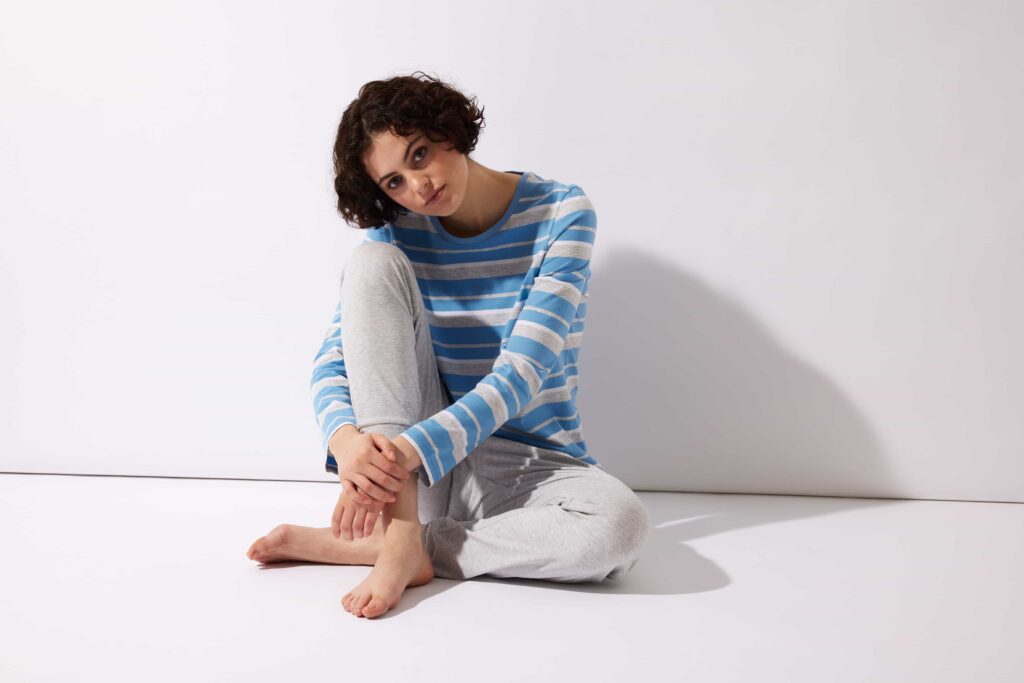 Frau in einem langen Schlafanzug sitzt auf dem Boden.