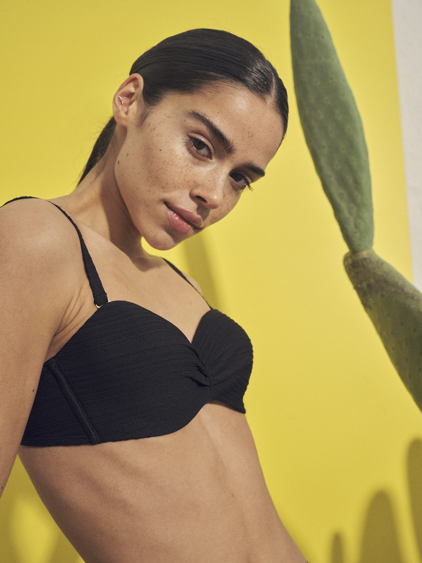 Model in einem schwarzen SCHIESSER Badeau Bikini vor einer gelben Wand