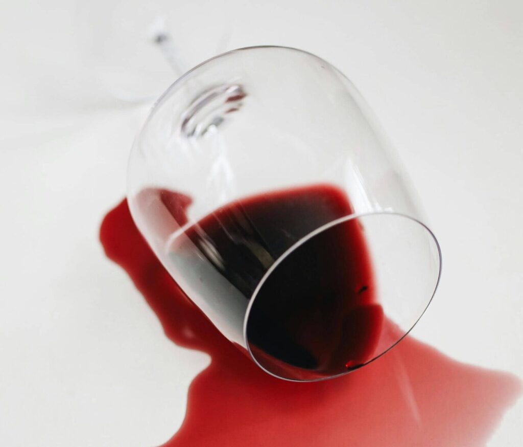 Verschütteter Rotwein aus einem umgekippten Glas auf heller Fläche.