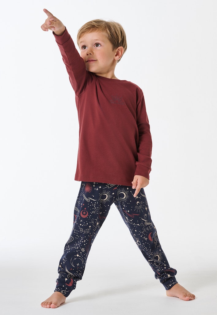 Junge in einem SCHIESSER Pyjama. Das Unterteil ist mit Sternen und einem Mond in Blau. Das Oberteil ist rot.