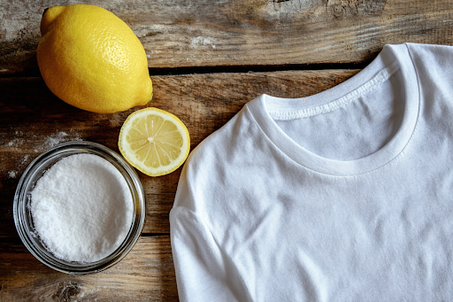 Zitrone, Natron und weißes T-Shirt auf Holztisch – Hausmittel, um Schweißgeruch aus Kleidung zu entfernen.