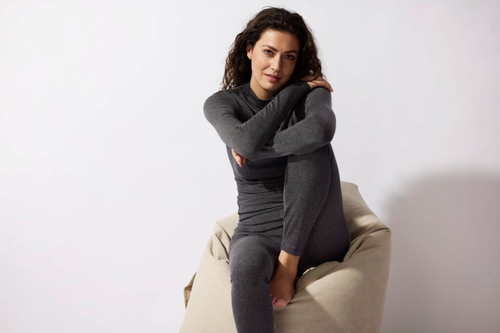 Weibliches Model sitzt auf einem beigen Sitzsack in grauer SCHIESSER Kleidung