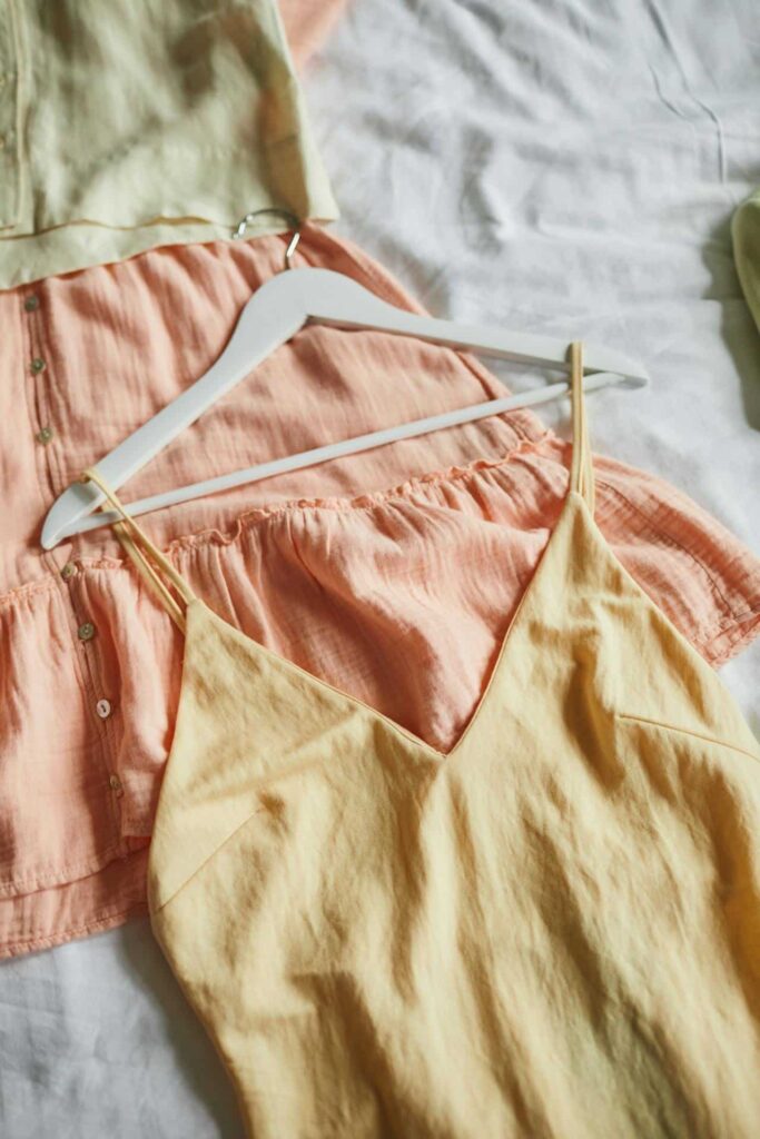Zwei sommerliche Kleidungsstücke in Pastellfarben auf Kleiderbügeln, ein gelbes Top und ein apricotfarbenes Kleid