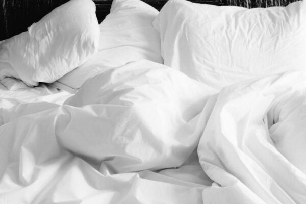 Weiße Bettwäsche liegt nach dem Schlafen offen auf dem Bett zum Lüften.