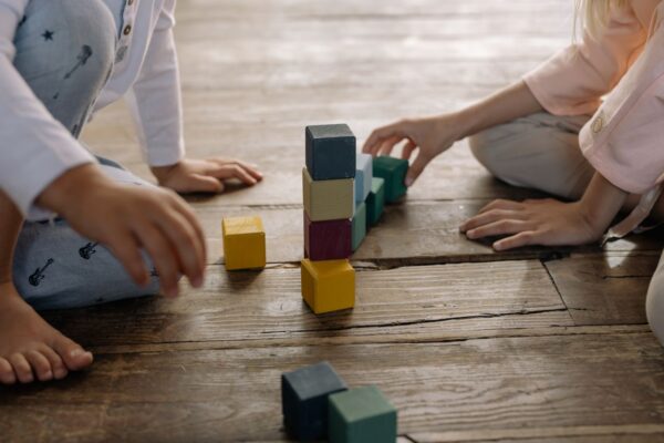 Kinder spielen gemeinsam mit bunten Bauklötzen auf dem Boden.